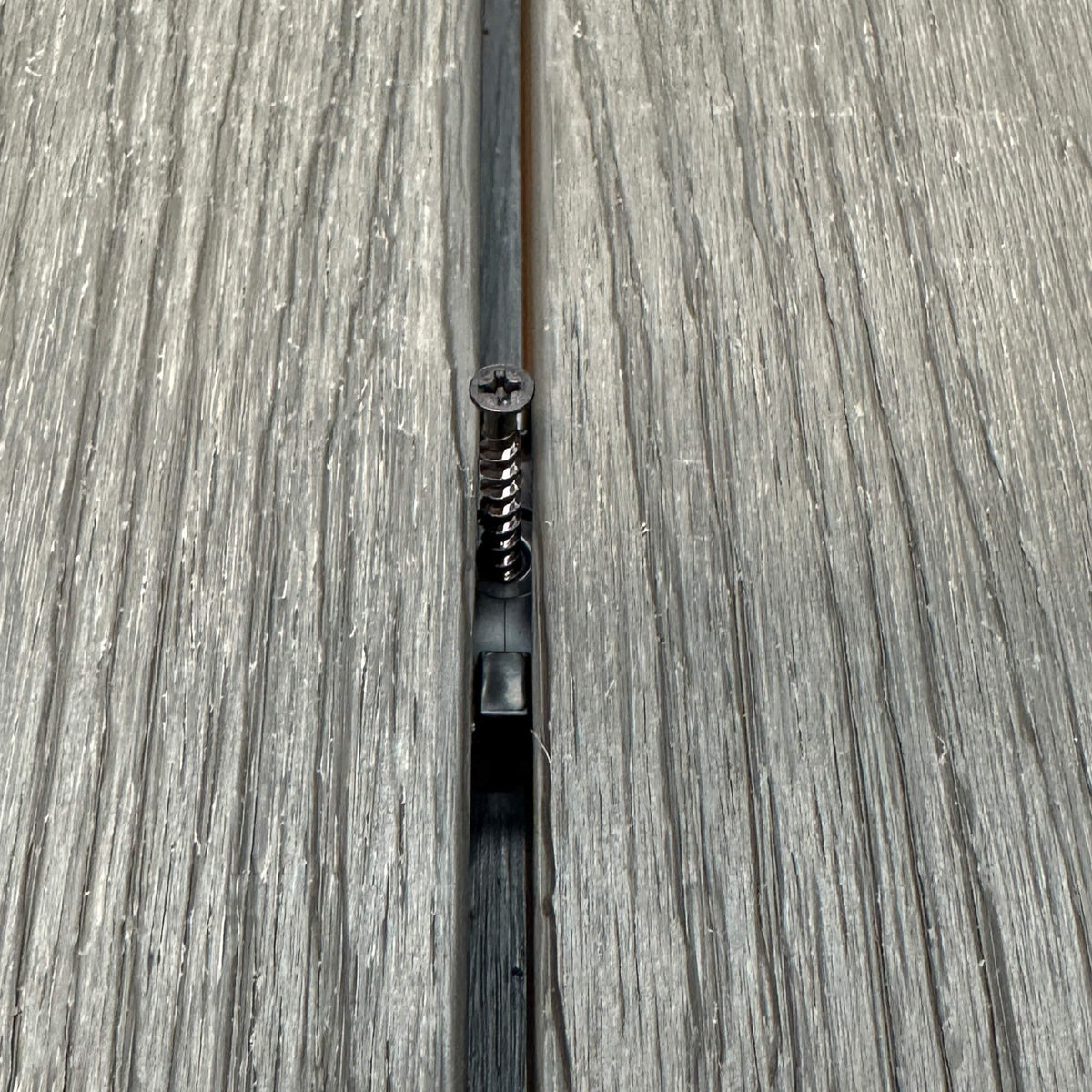 A Black Decking Clip & Screw in situ on a decking patio background.