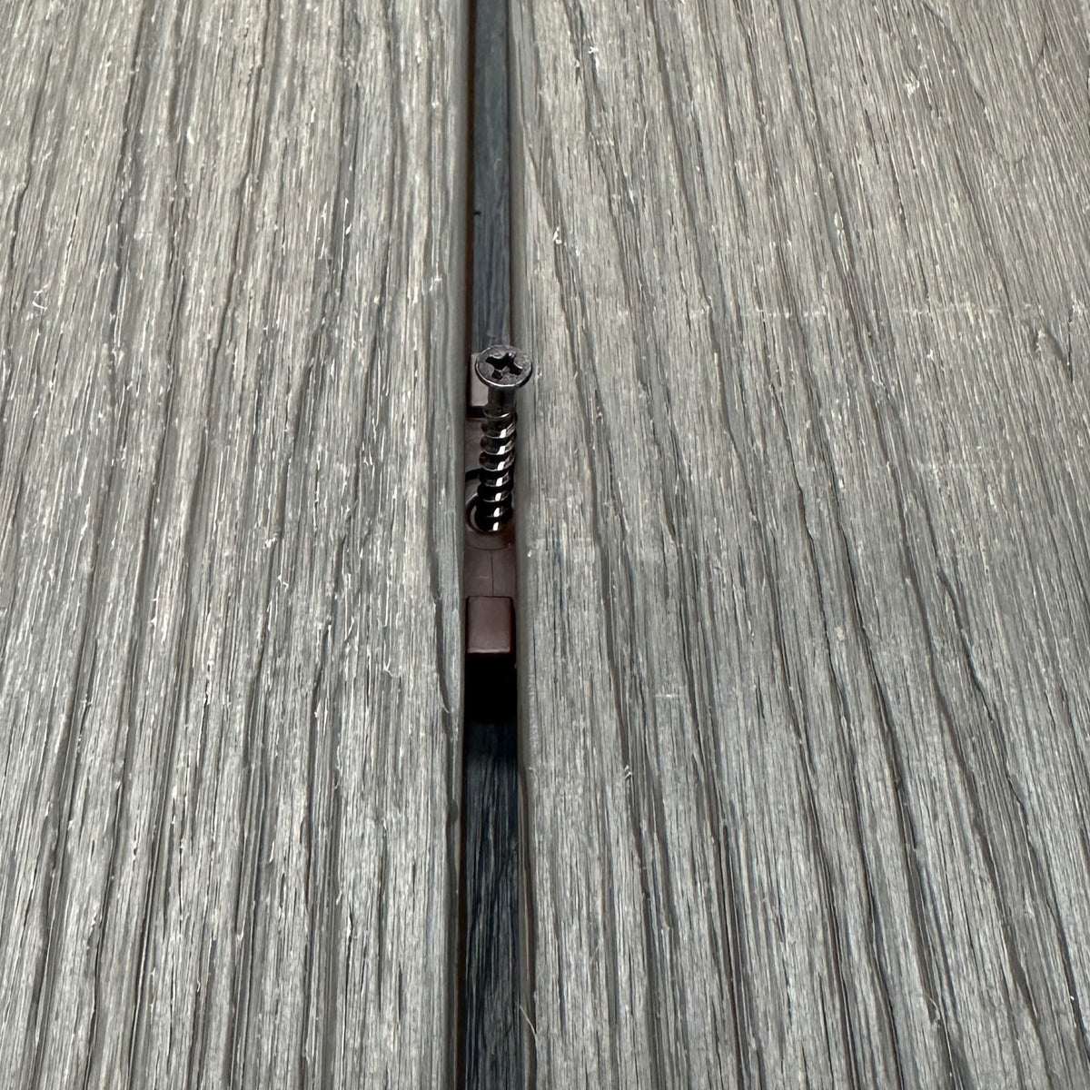 A Brown Decking Clip & Screw in situ on a decking patio background.
