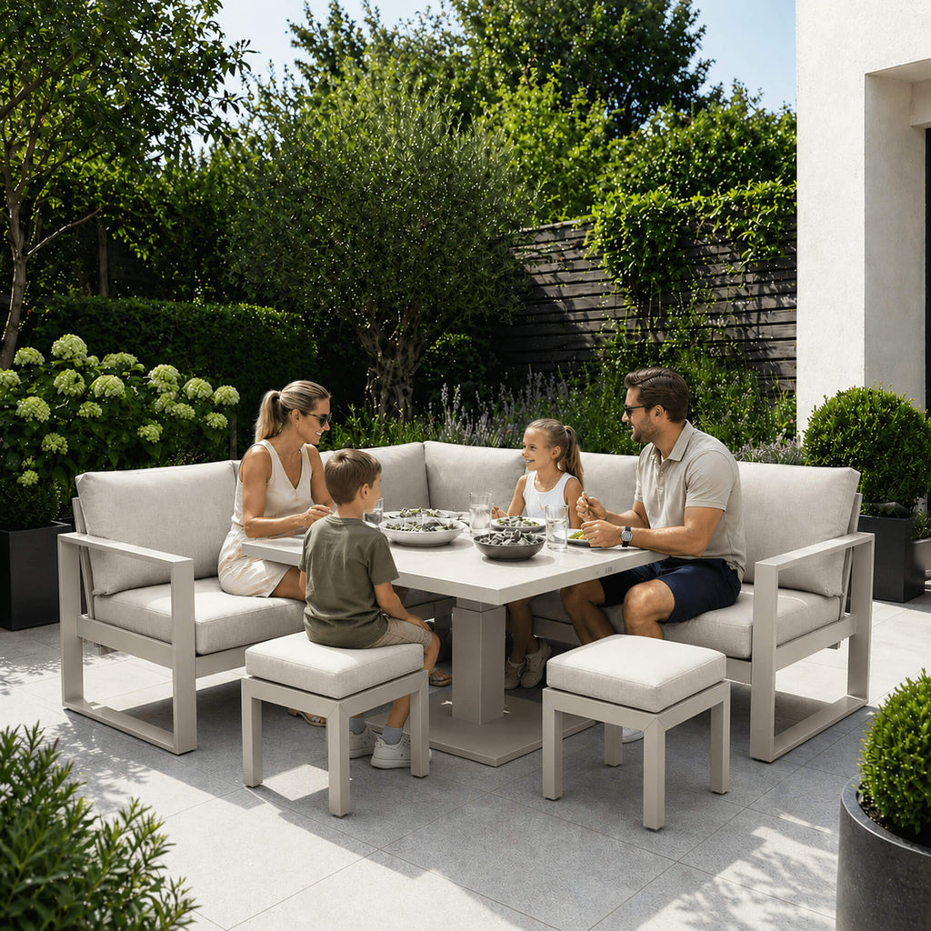 Family sitting on a patio with the Como stone corner set and accompanying foot stools surrounded by greenery.