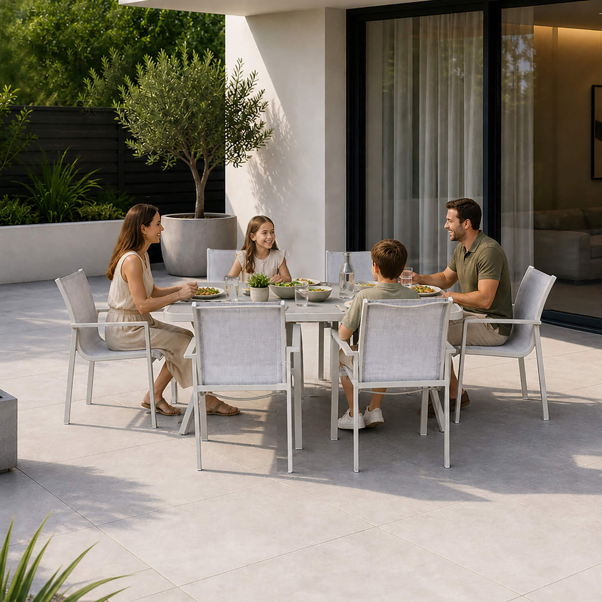 A family of four sits at a Garda Stone Outdoor Dining Furniture Set with four matching outdoor mesh chairs on a modern patio. 